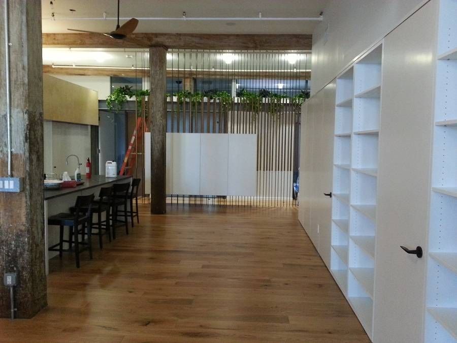 Spacious modern loft with wooden floors, white shelves, and a kitchen area with bar stools.