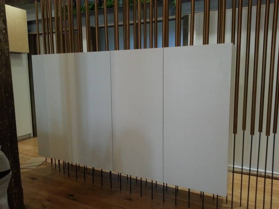 White panels in front of a backdrop of vertical bronze poles, standing on thin dark rods.