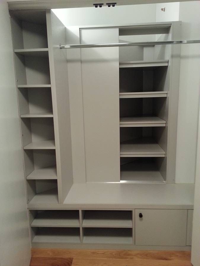 Empty gray closet with shelves, hanging rod, and a closed cabinet on a wood floor.
