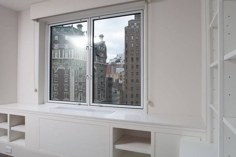 Window overlooking city buildings with white built-in storage below.
