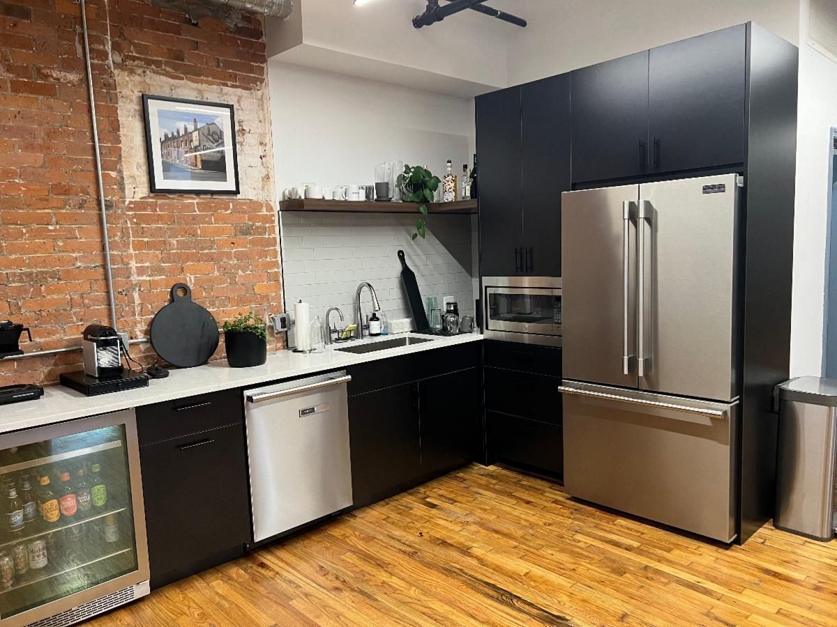 Modern kitchen with brick wall, black cabinets, stainless steel appliances, and wood floors.