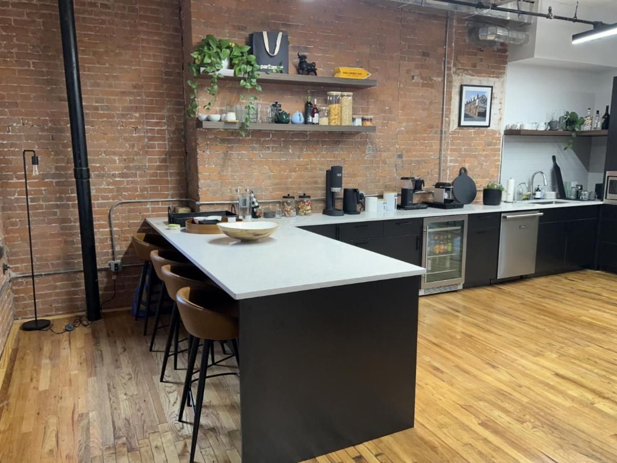 Industrial kitchen with brick wall, island, bar stools, shelves, and appliances.