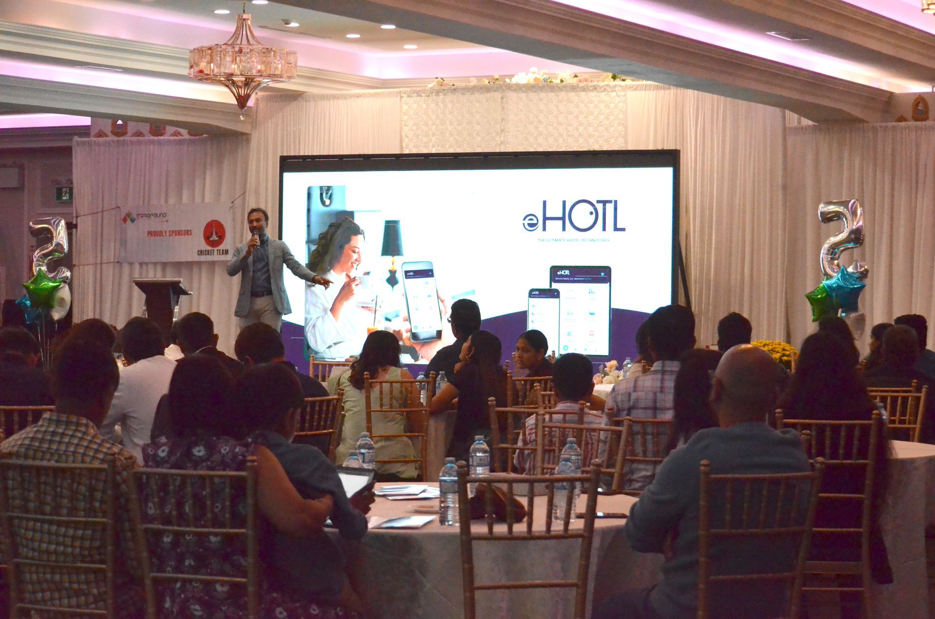 Audience watches a presentation on a large screen in a banquet hall.