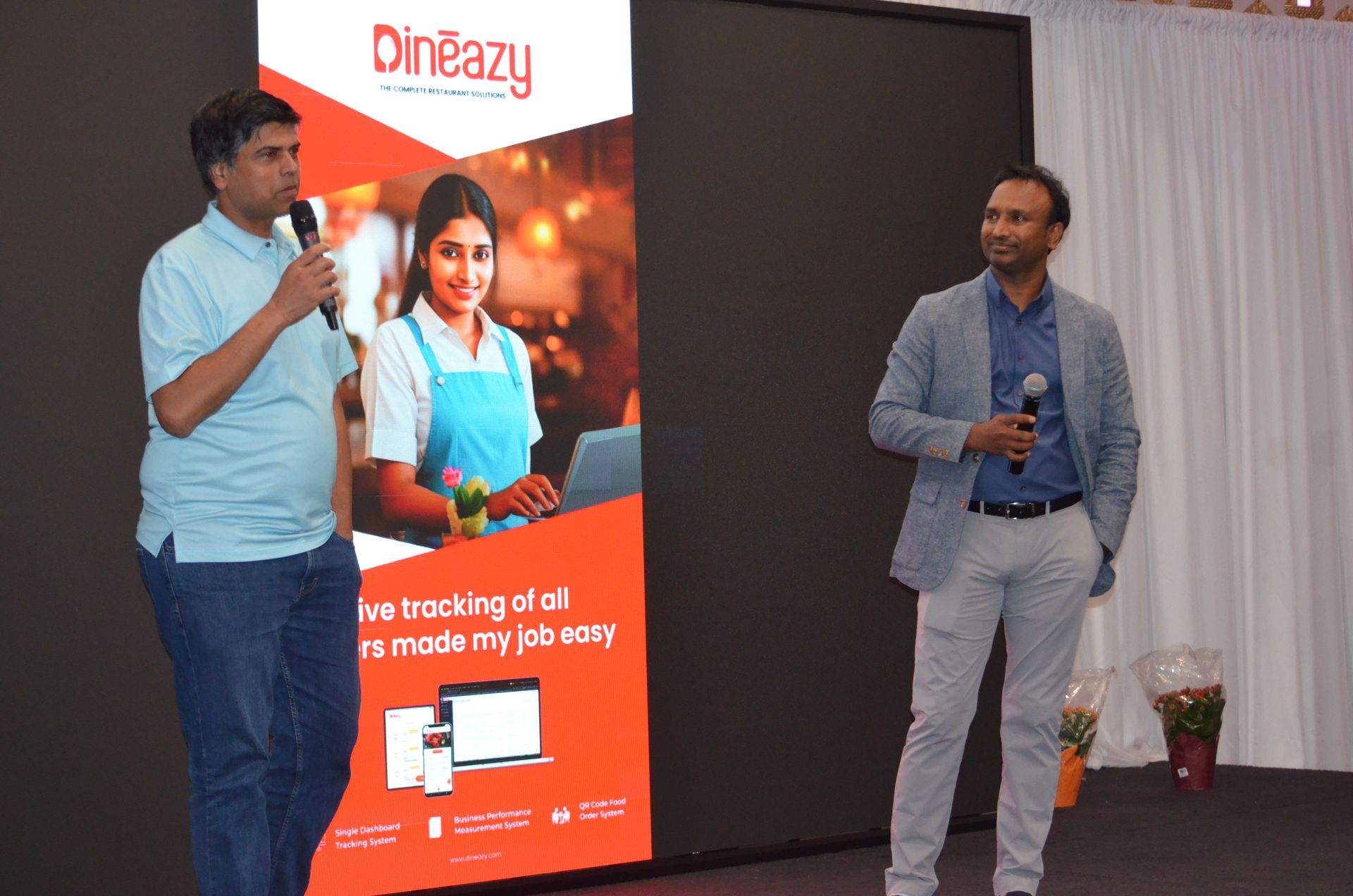 Two men speaking on a stage beside a DinEasy promotional banner
