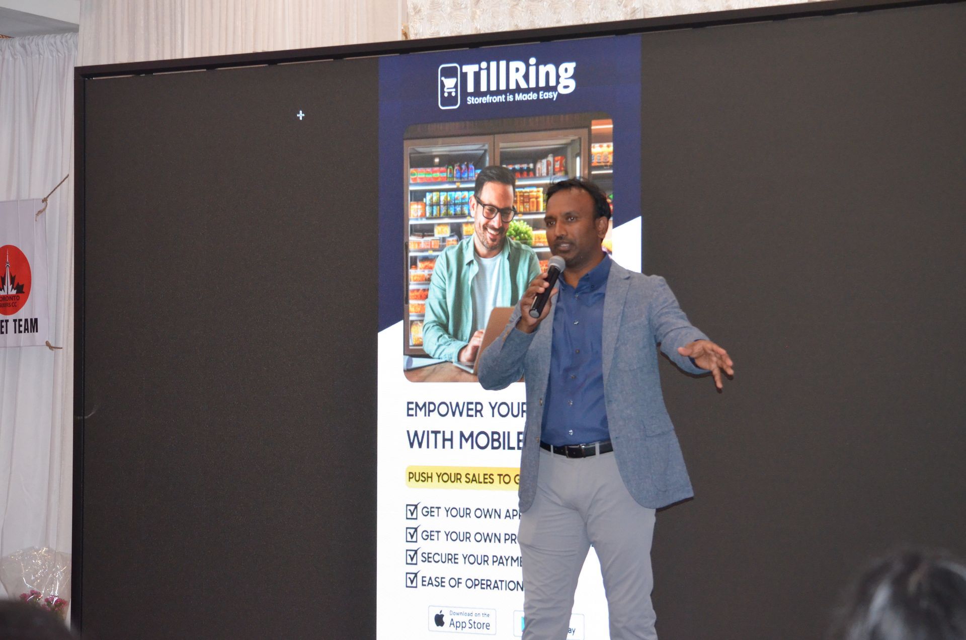Man speaking on stage beside a large screen, gesturing during a presentation.