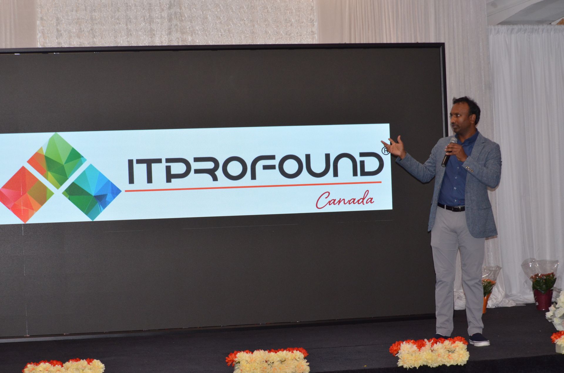 Speaker on stage beside ITProFound Canada banner, giving a presentation with hand gestures.