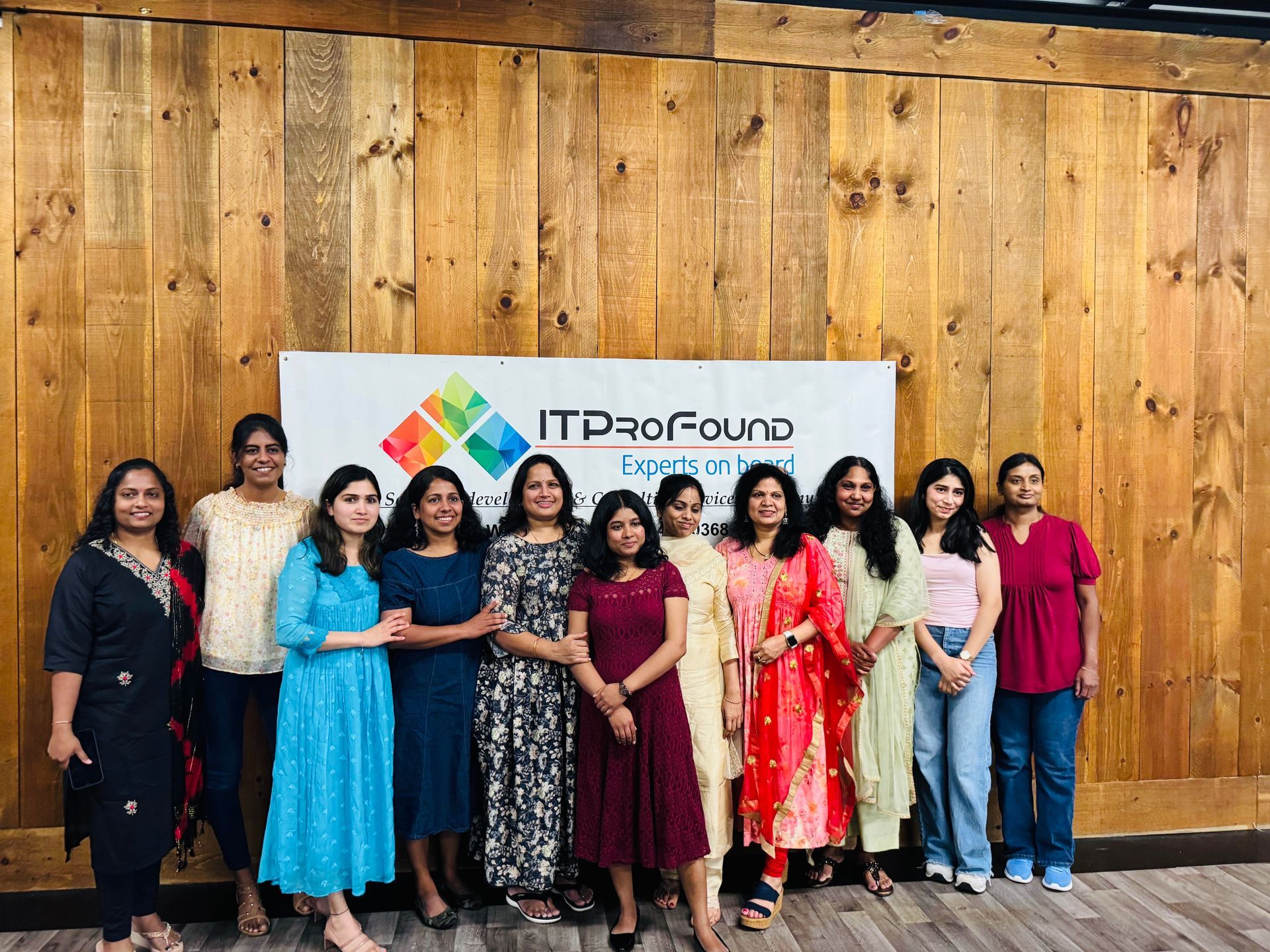 Group of people posing indoors in front of a wooden wall and “ITProFound” sign