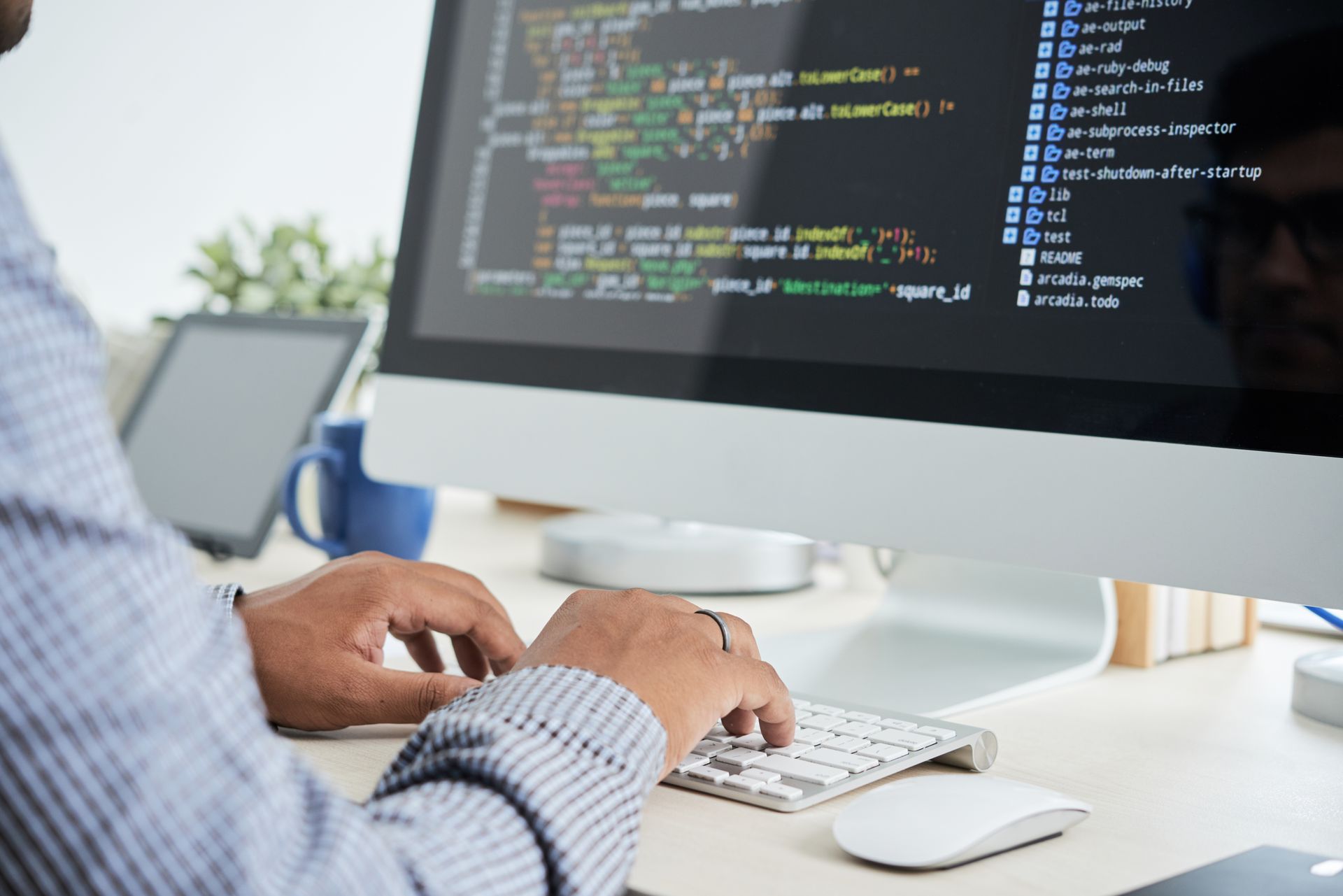 Person typing at a desktop computer displaying code in a bright office workspace