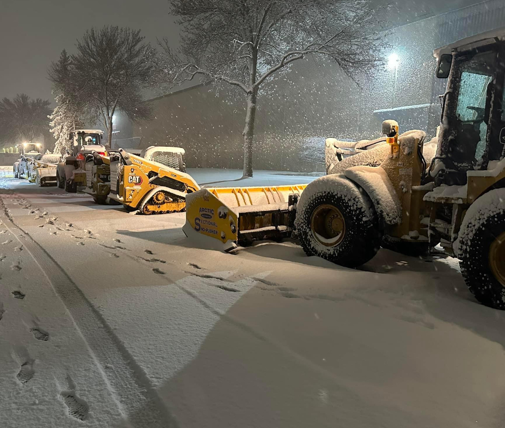 A snow plow is parked on the side of the road at night.