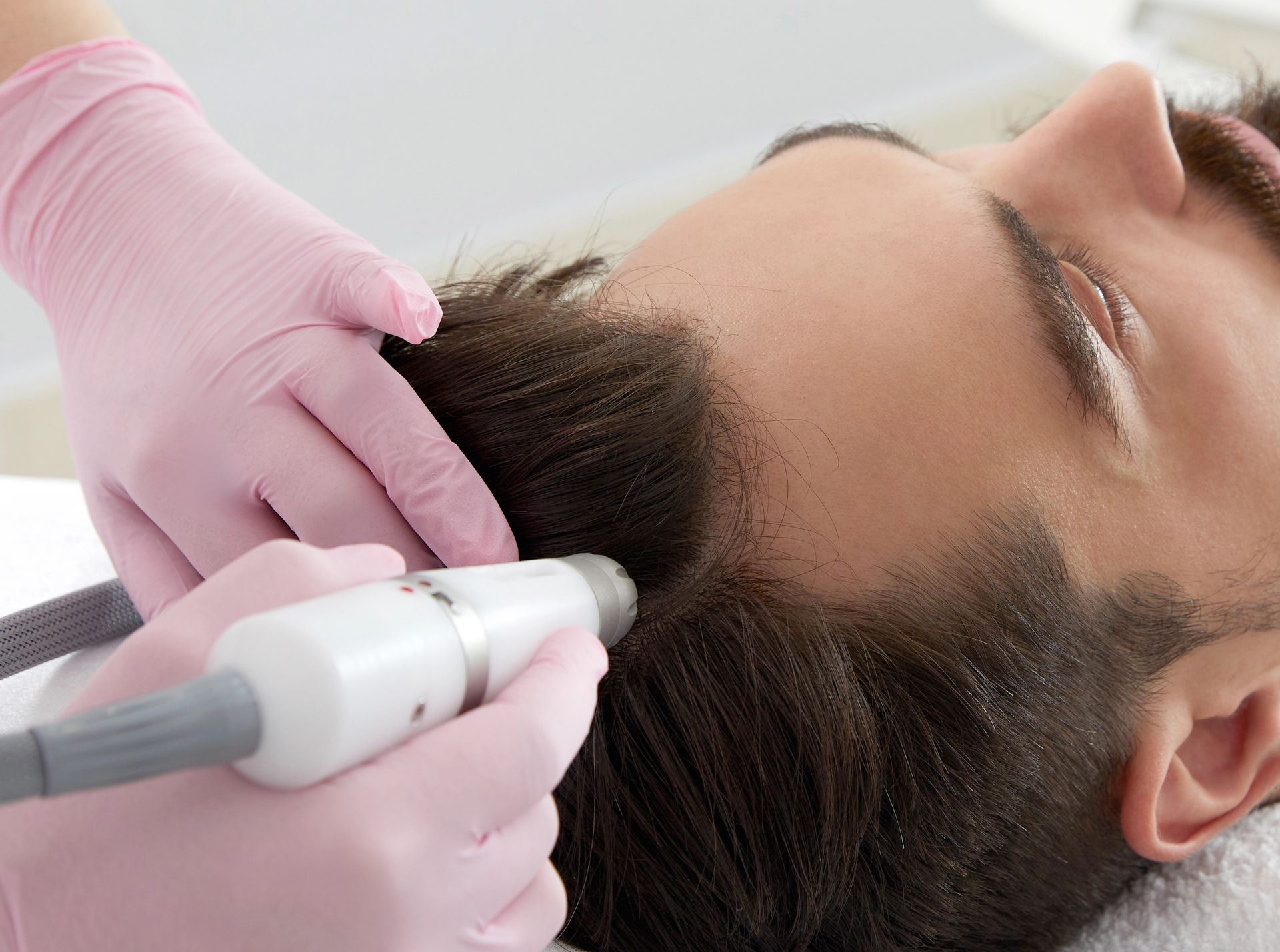 Un professionista con indosso guanti rosa utilizza un dispositivo cosmetico portatile per trattare il cuoio capelluto di una persona.