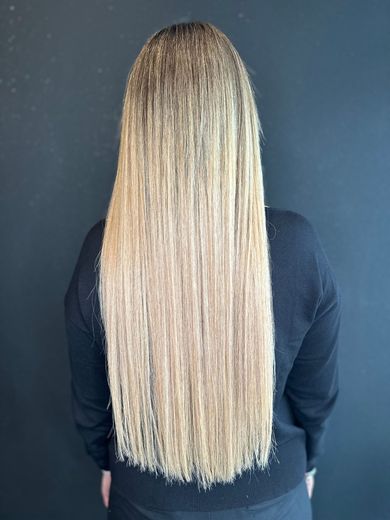 Una persona, vista di spalle, mostra lunghi capelli biondo chiaro, dall'aspetto mosso e crespo, sullo sfondo di una semplice parete scura.