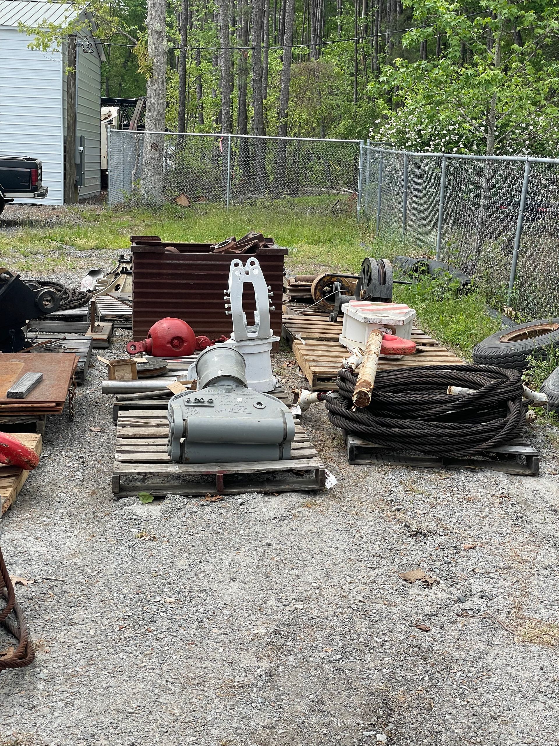 Equipment parts, including a large gray gearbox, on pallets outdoors in a gravel area.