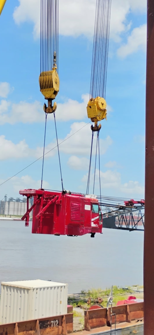 Red container lifted by two yellow crane hooks against a blue sky.