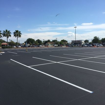 Worker using line striping machine to apply white line on asphalt parking lot for traffic control
