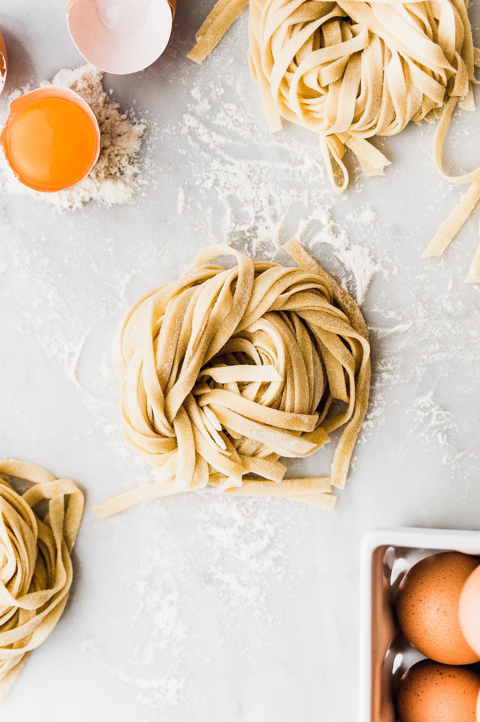 Nidos de pasta fresca e ingredientes sobre una superficie enharinada; huevos, yema y harina.