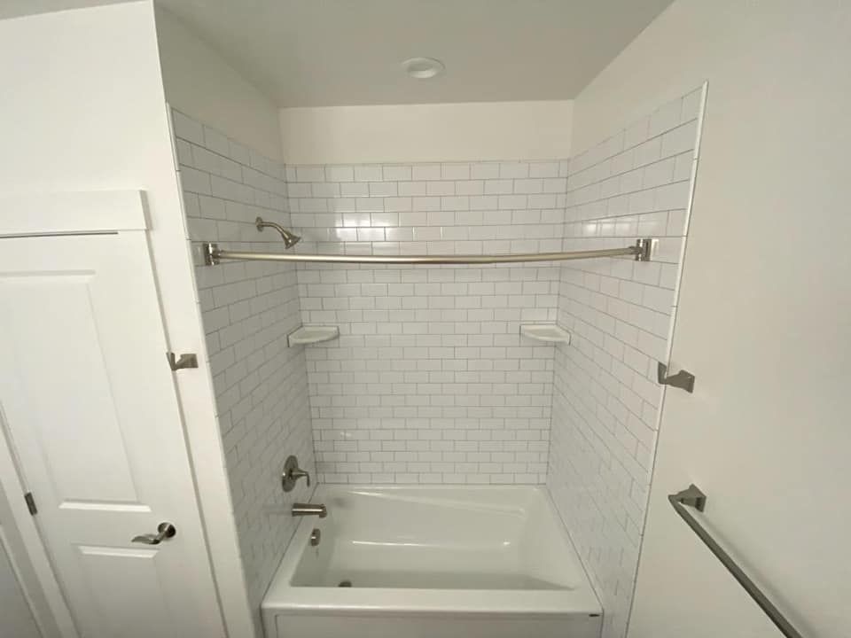 Accessible bathroom with white-tiled tub shower, grab bars, and built-in seat.