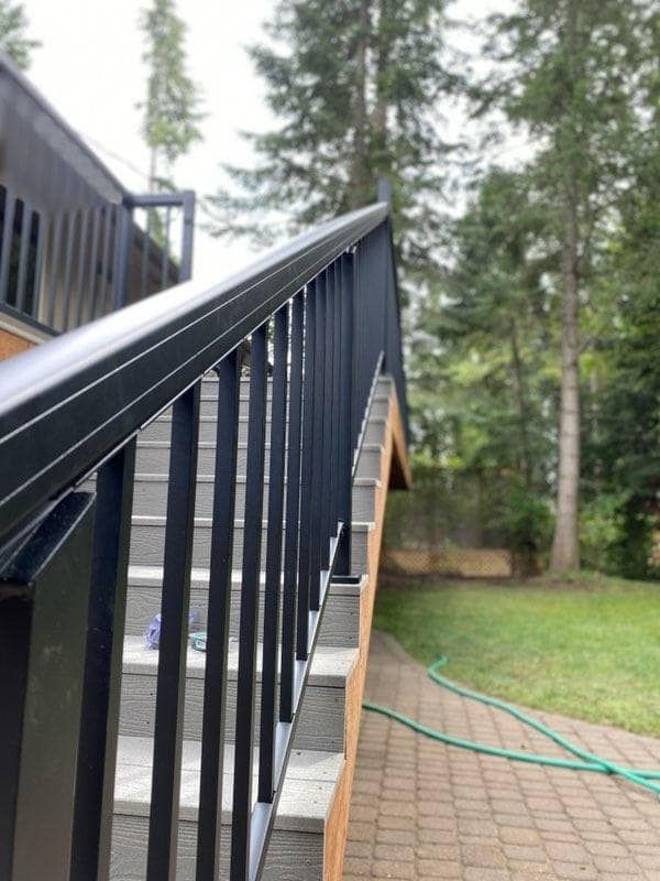 Black metal stair railing beside a brick patio, with green garden hose and trees in the background