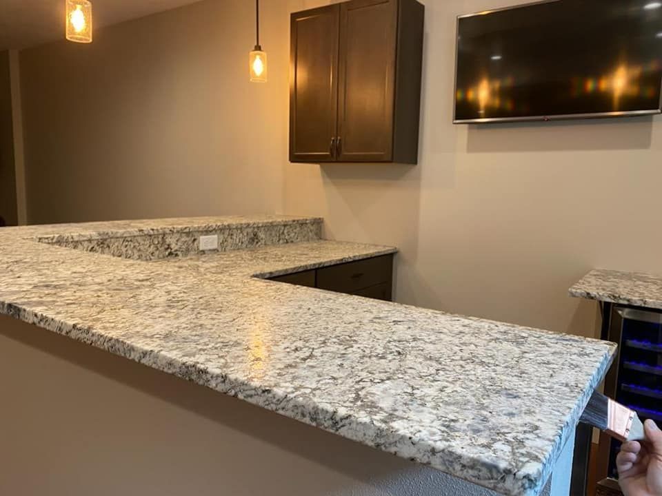 Empty kitchen with granite island countertop, dark cabinets, pendant lights, and a wall-mounted TV