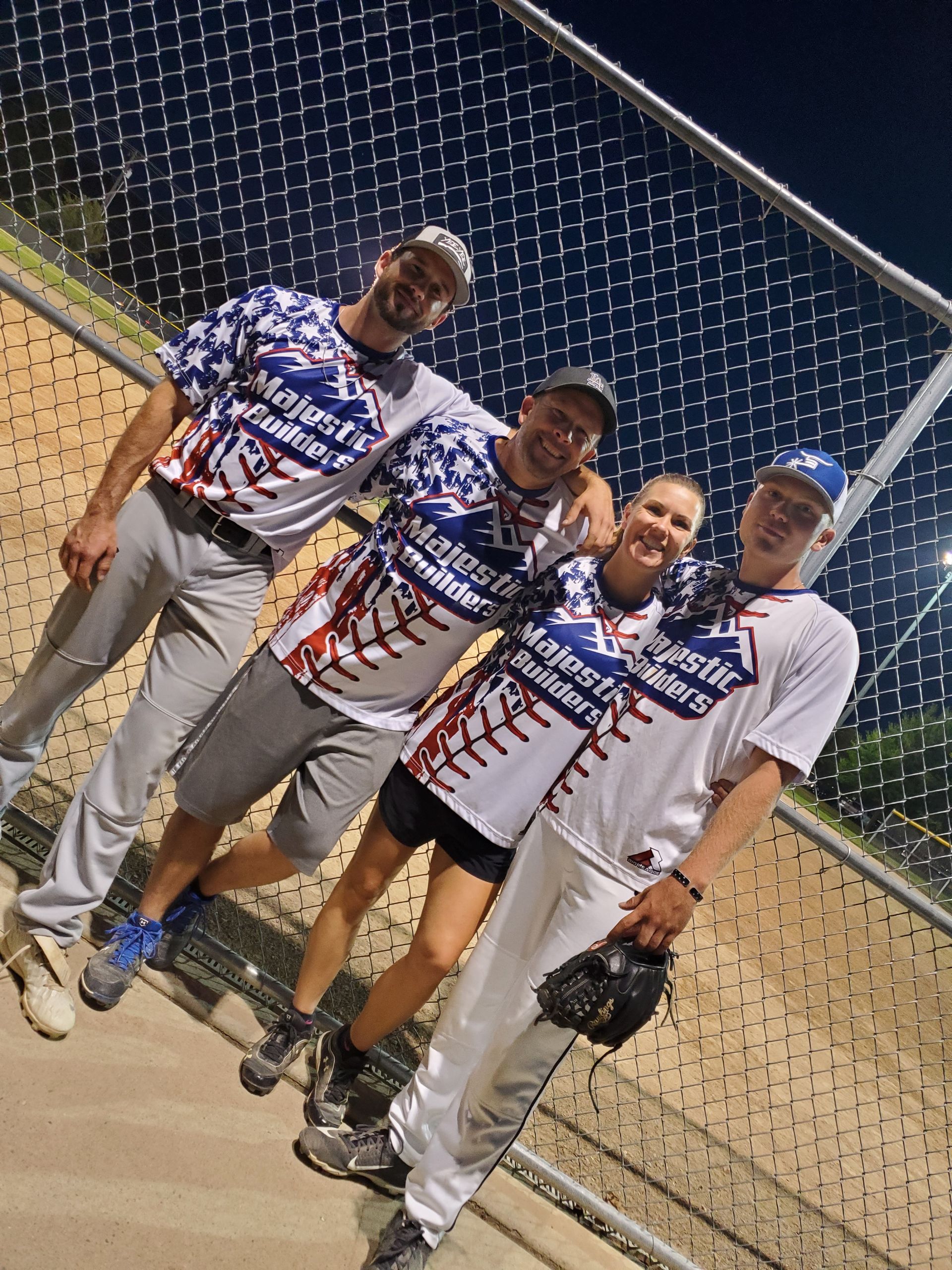 Four baseball players in white and blue jerseys pose on a field behind a chain-link fence.