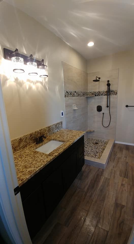 Modern bathroom with granite vanity, wall lights, and walk-in shower with tiled bench