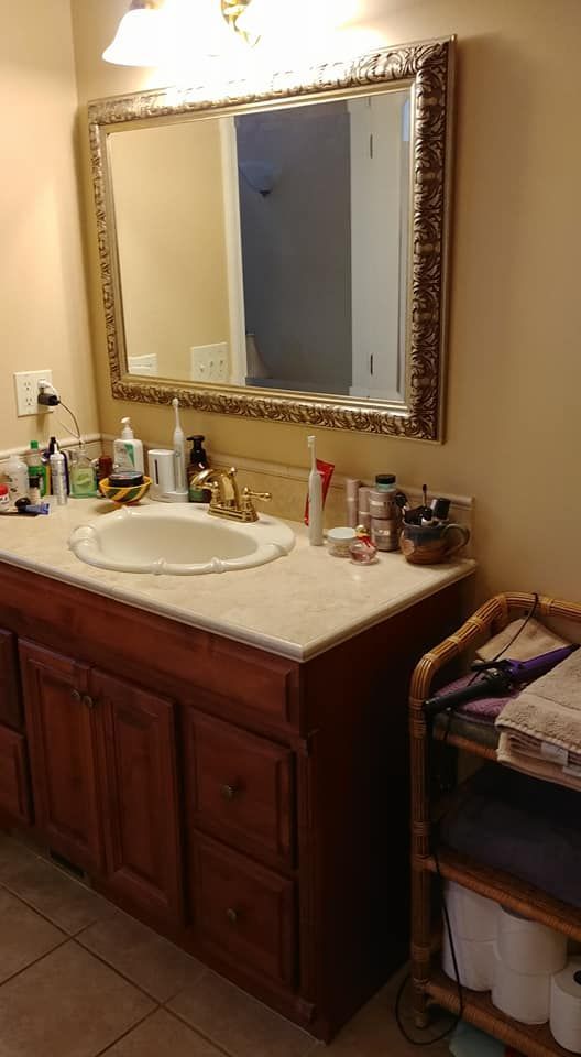 Bathroom vanity with sink, mirror, toiletries, and wooden cabinet beside a tiled floor.