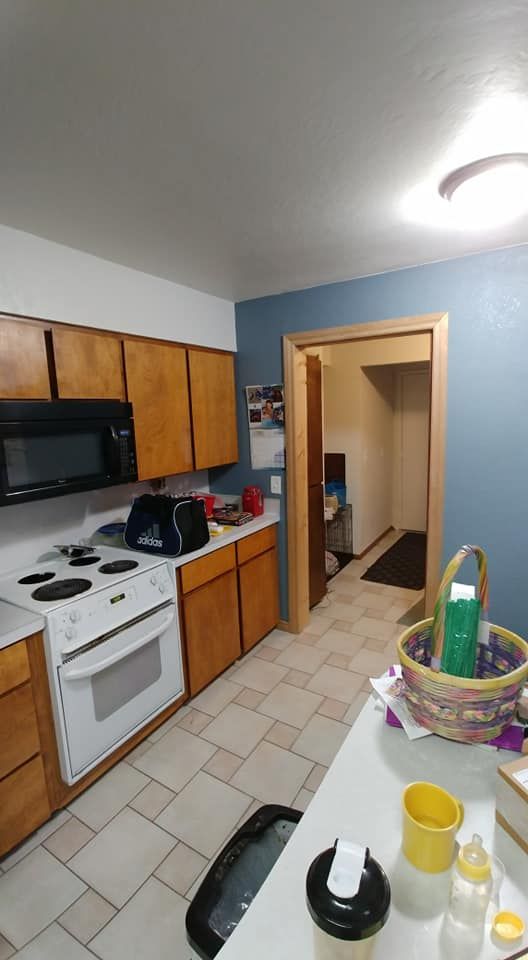 Small kitchen with wood cabinets, white stove, blue walls, tiled floor, and a doorway to a hallway.