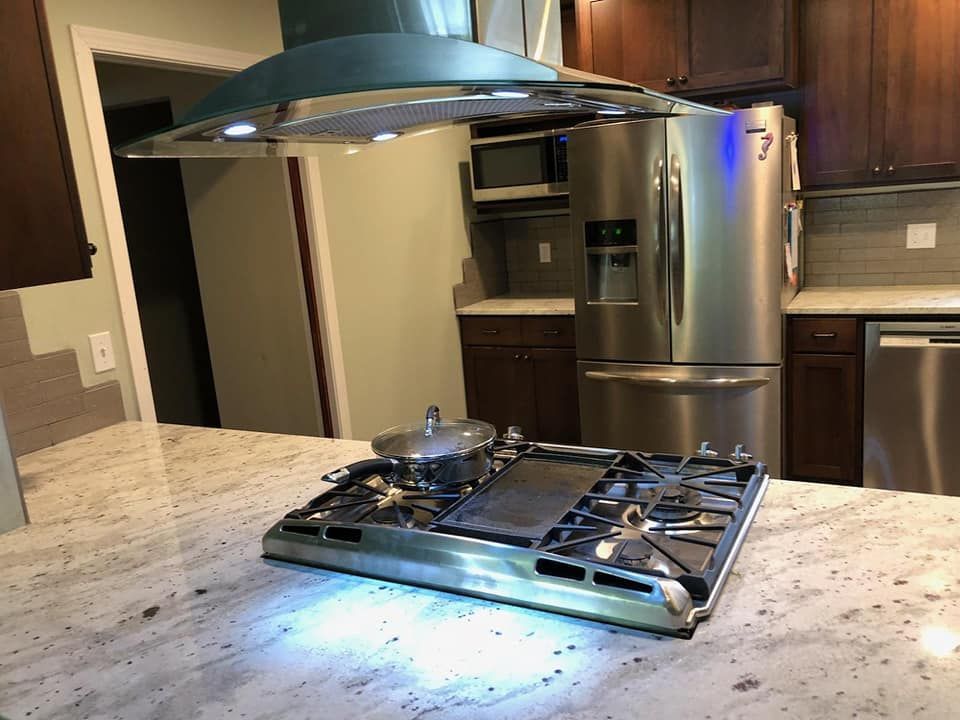 Modern kitchen with stainless steel appliances and a gas cooktop on a granite island under a range hood