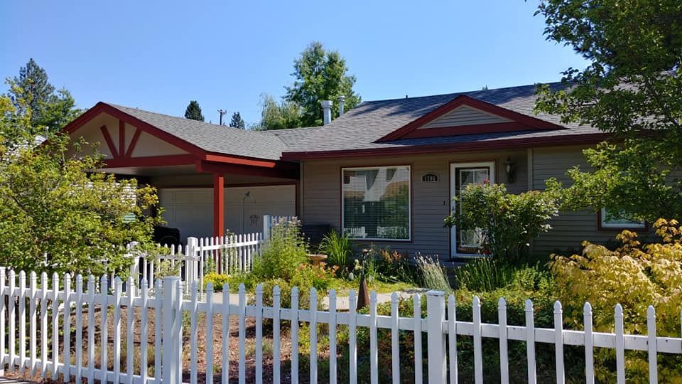 Single-story house with a white picket fence, red trim, and a front yard under a clear blue sky