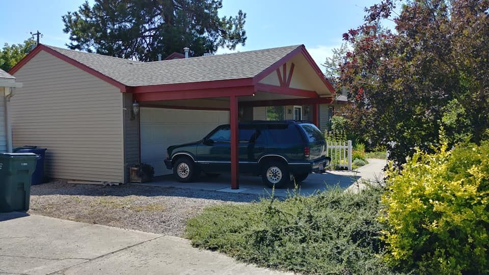 Carport with red trim and a blue SUV parked beside a beige house on a sunny day