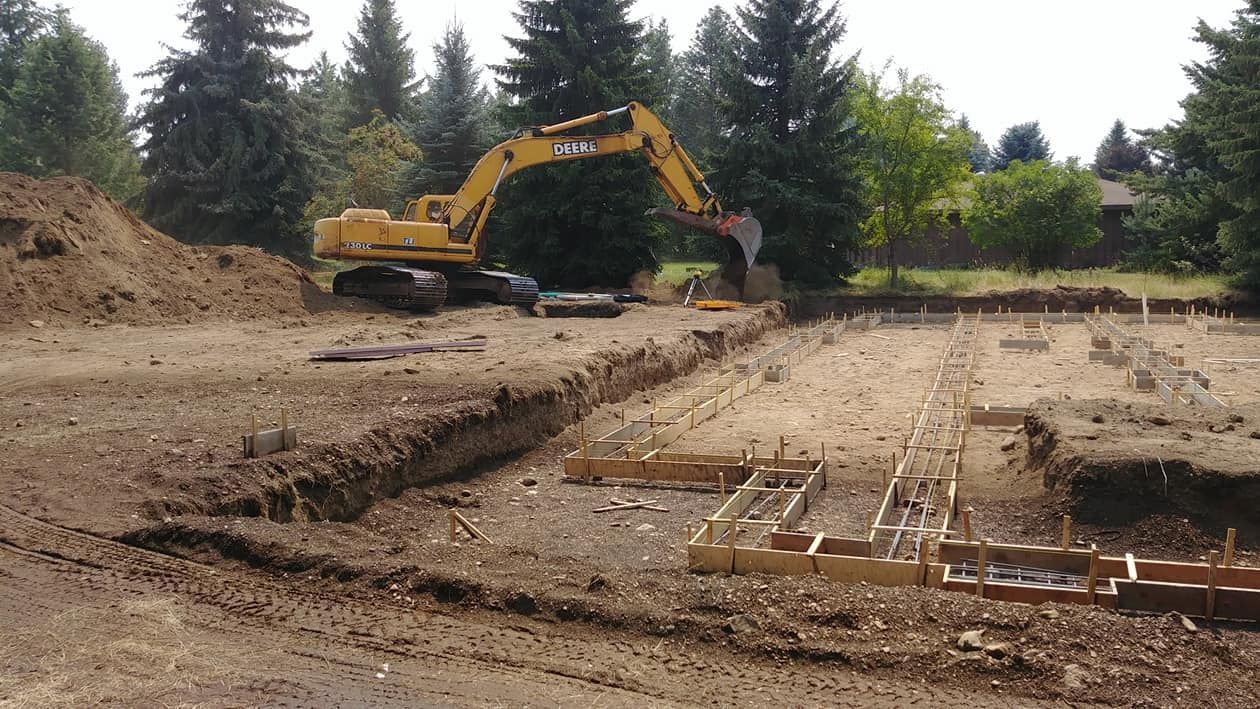 Yellow excavator digging at a construction site with dirt piles and foundation forms