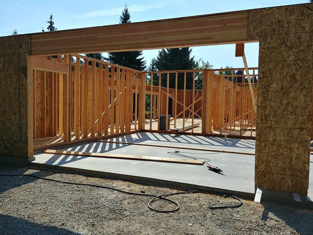Framed house under construction with wooden walls and roof trusses on a concrete slab