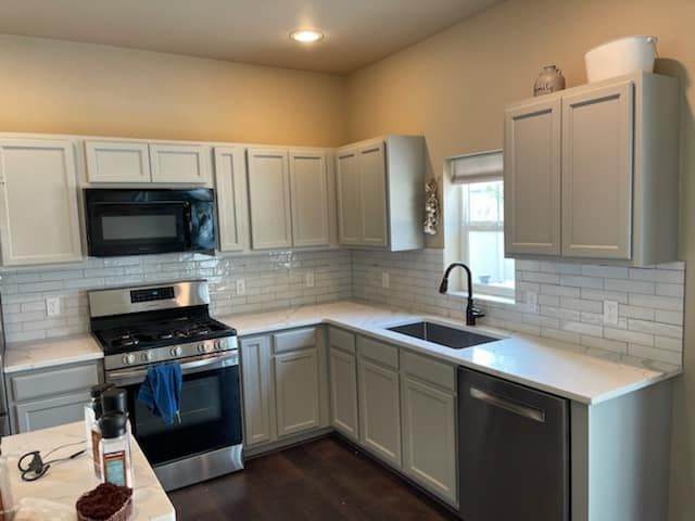 Modern kitchen with white cabinets, stainless steel appliances, gray counters, and a tiled backsplash