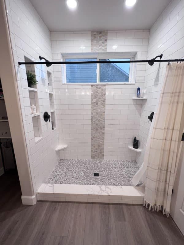 Walk-in tiled shower with black grab bar, built-in niches, and striped curtain in a modern bathroom.