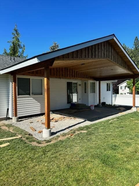 Covered front porch with wooden roof, white siding, and a grassy yard in bright sunlight