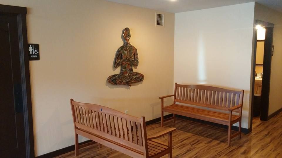 Waiting area with wooden benches, wall art, and a doorway in a beige hallway.