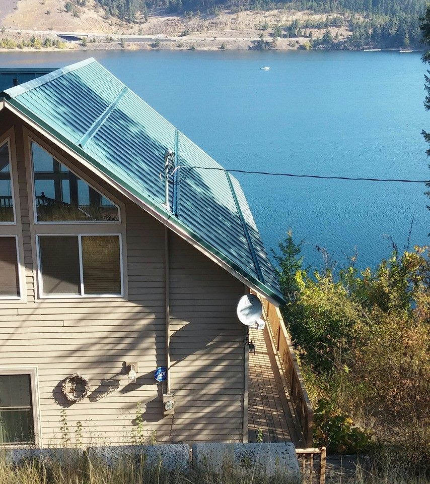 House with blue roof beside a lake, with trees and hills in the background