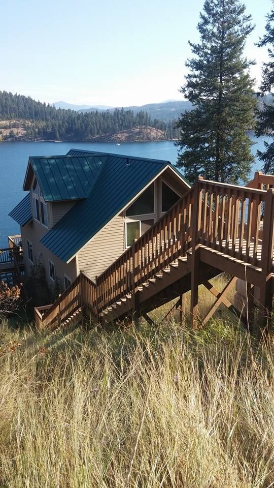 Wooden stairs beside a blue-roofed lakeside cabin, overlooking water and trees on a sunny day