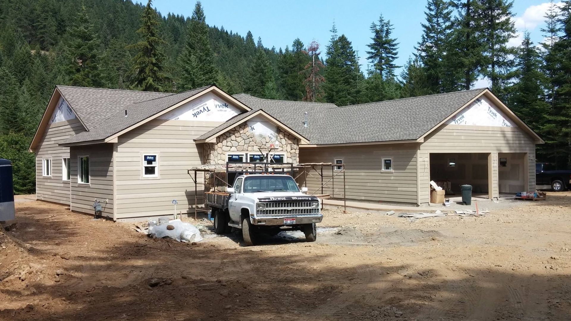 New house under construction with a white pickup truck parked in front, surrounded by trees