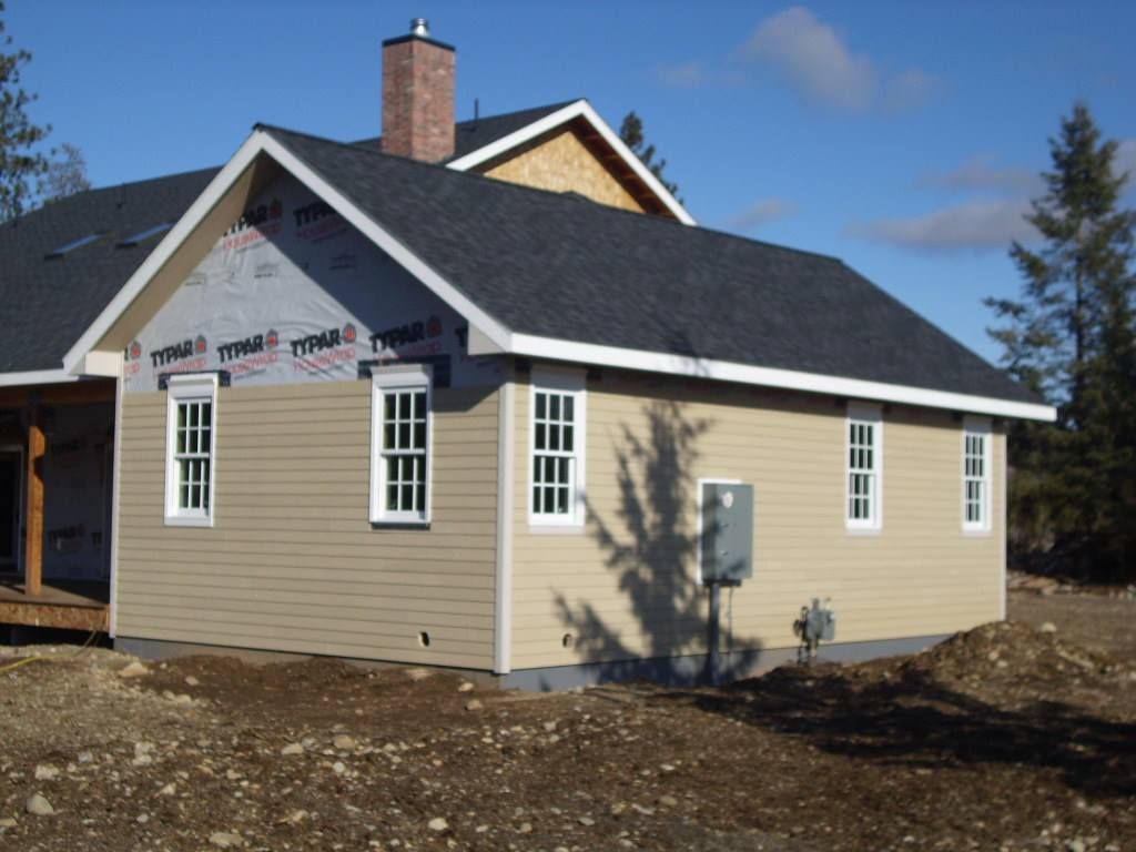 Single-story beige house with white trim, dark roof, and stone chimney under a blue sky