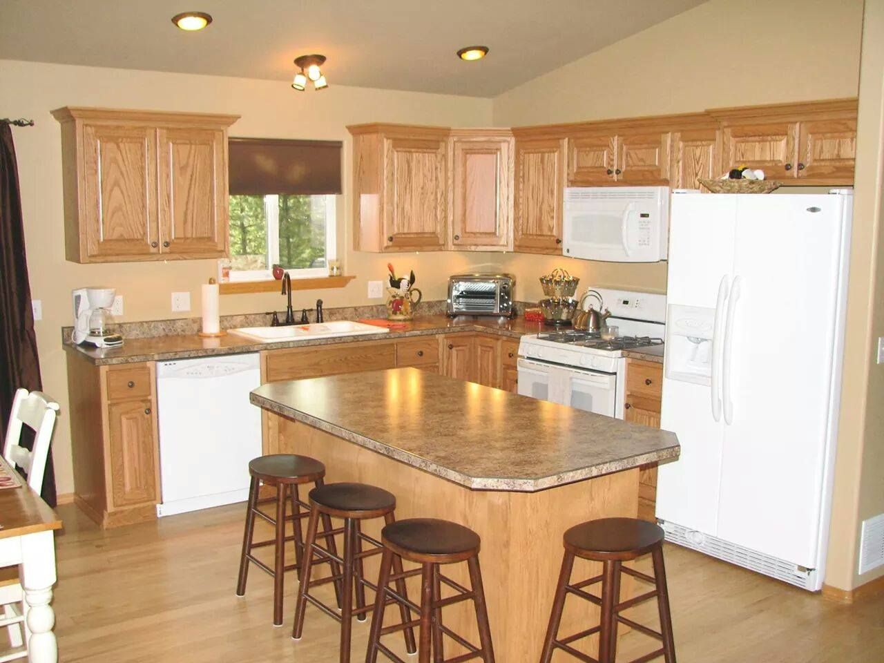 Spacious kitchen with wood cabinets, granite island, white appliances, and three stools.
