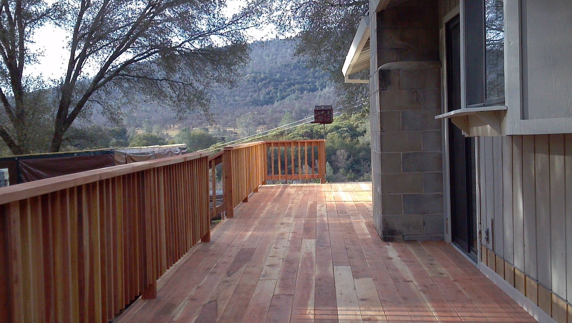 Wooden deck with railing beside a house, overlooking trees and mountains in the distance