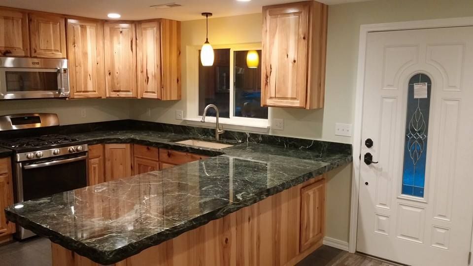 Modern kitchen with wooden cabinets, black granite island, and white door with blue glass panel