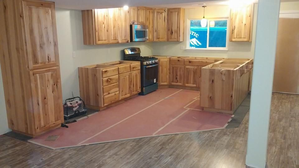 Empty kitchen with wood cabinets, black stove, pink flooring, and a window over the sink.