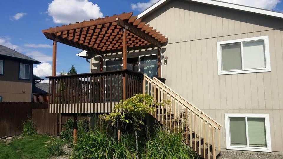 Back deck with pergola and stairs beside a beige house, overlooking a grassy yard