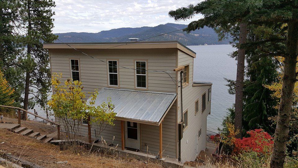 White house on a wooded hillside overlooking a lake, with mountains in the distance