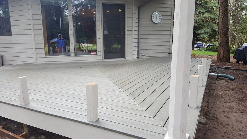 White wooden deck beside a gray house with sliding glass doors and white railings.