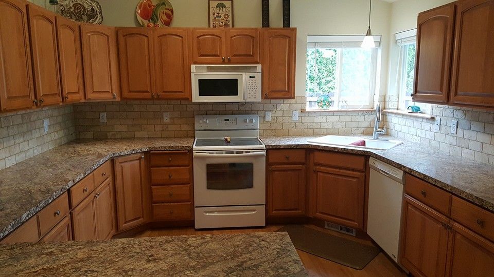 Empty kitchen with wooden cabinets, granite counters, white tile backsplash, and stainless steel stove and microwave.