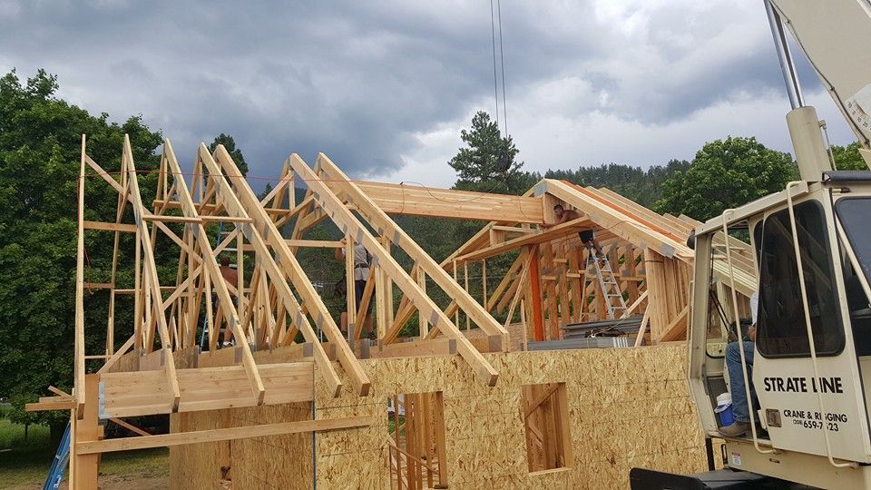 House framing under construction with wooden roof trusses and a work truck nearby