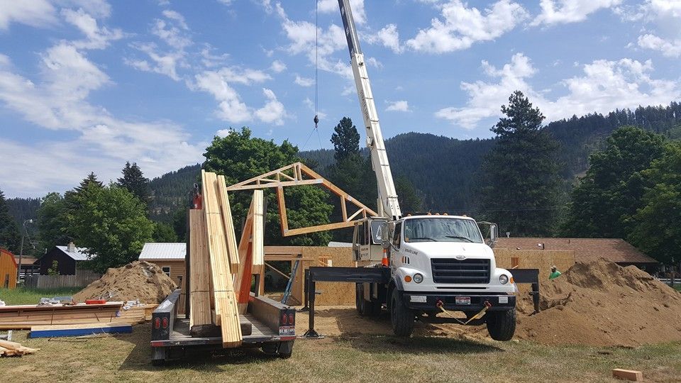 Truck lifting a wooden frame at a rural construction site with hills in the background
