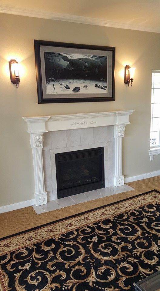 Elegant living room wall with white fireplace, framed artwork, wall sconces, and patterned rug.